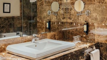 Een badkamer met een witte wasbak, een marmeren aanrechtblad, twee wandspiegels en een gecertificeerd document aan de muur.