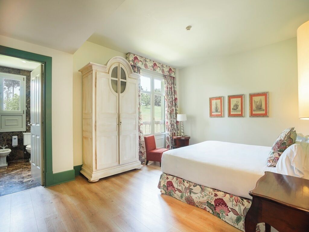Ein Schlafzimmer mit Bett, Kleiderschrank, Sessel und einem fenster mit Vorhängen.