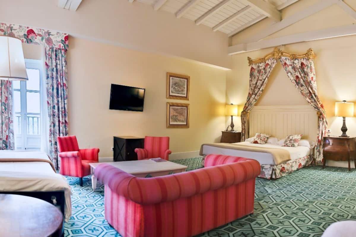 Una habitación de hotel con una cama, dos sillones, una mesa, un televisor y una cama con dosel.