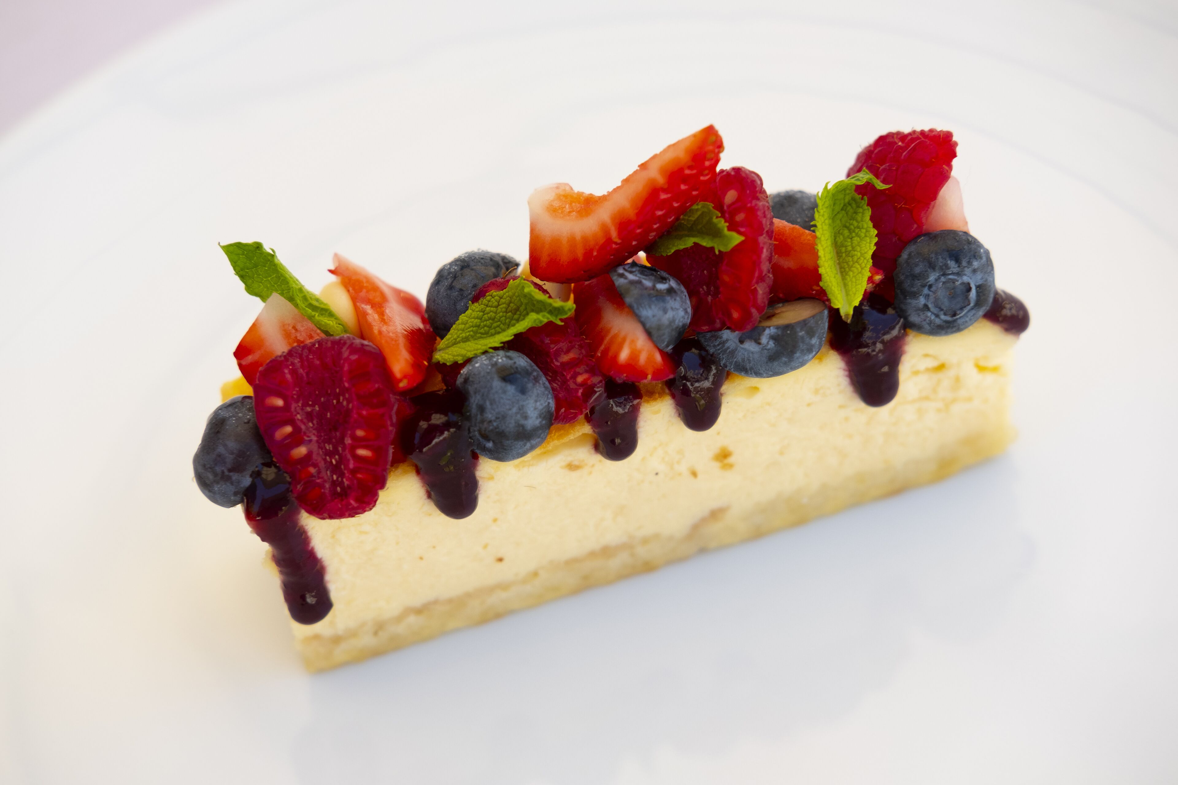 A slice of cheesecake topped with strawberries, blueberries, raspberries, and a mint leaf.