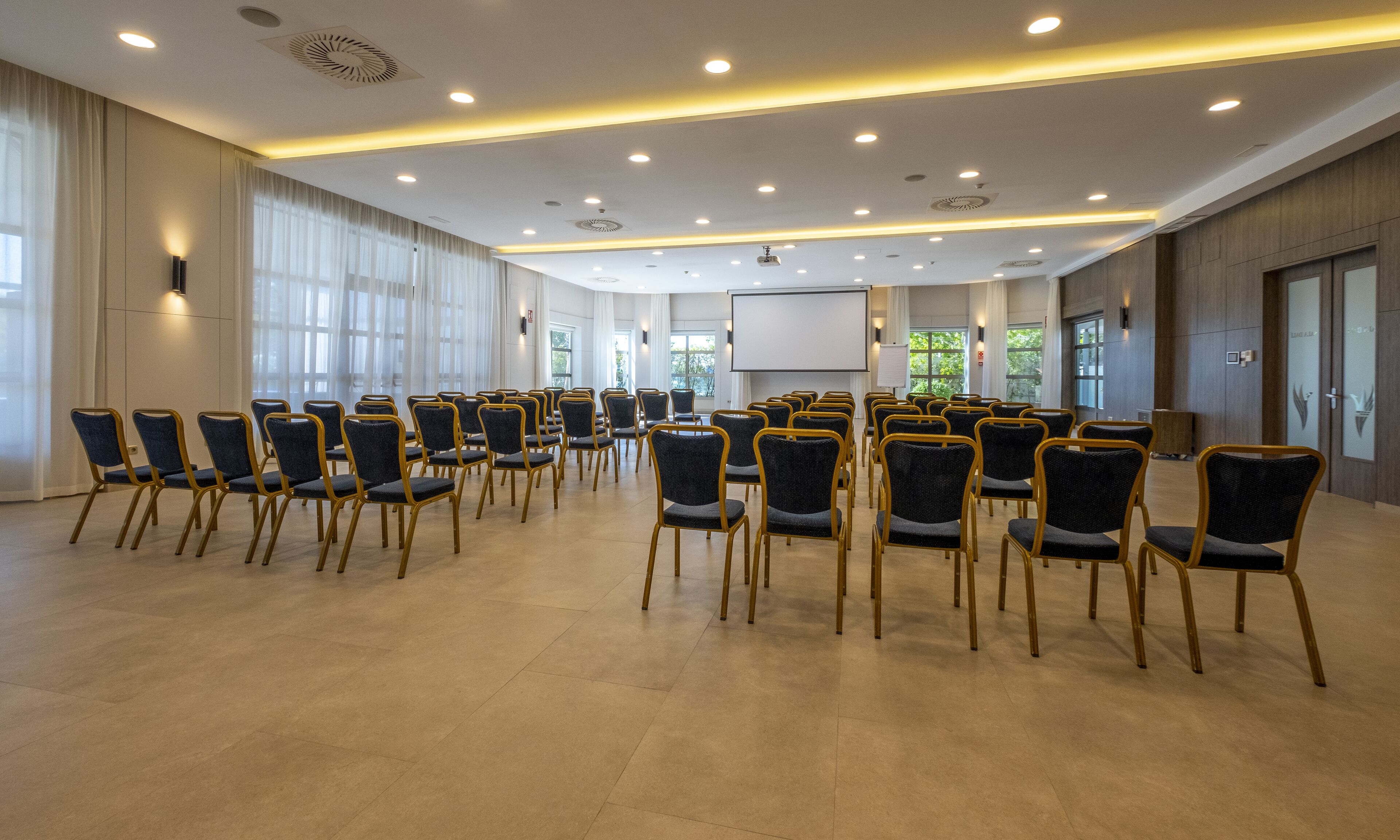 A conference room with rows of chairs, a projector screen, and a large window.