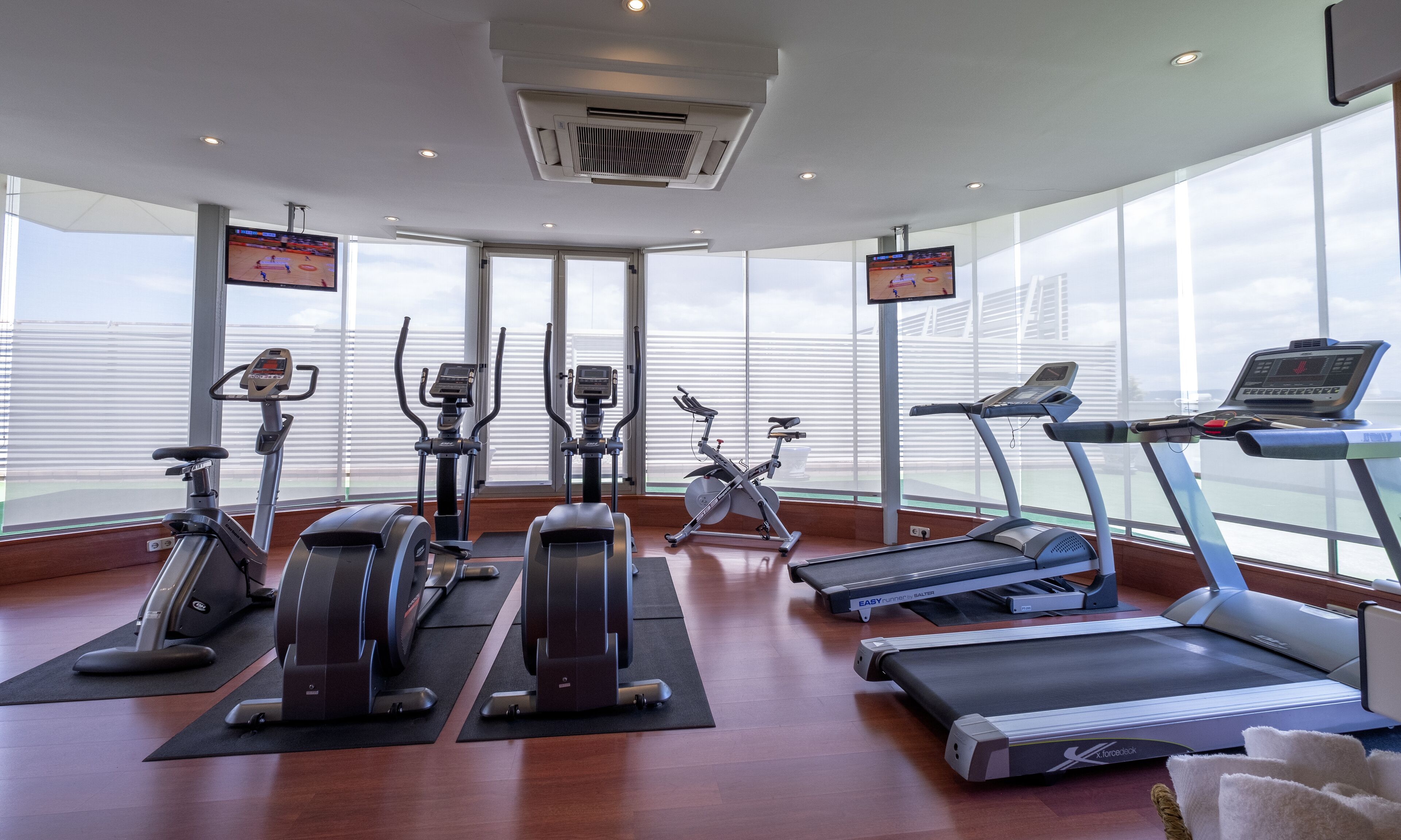 Een sportschool met diverse fitnessapparaten, grote ramen en uitzicht op de lucht.