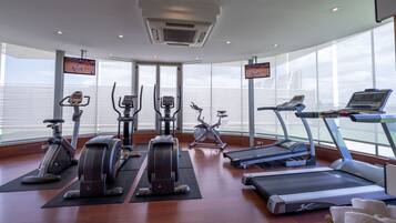 Een sportschool met diverse fitnessapparaten, grote ramen en uitzicht op de lucht.
