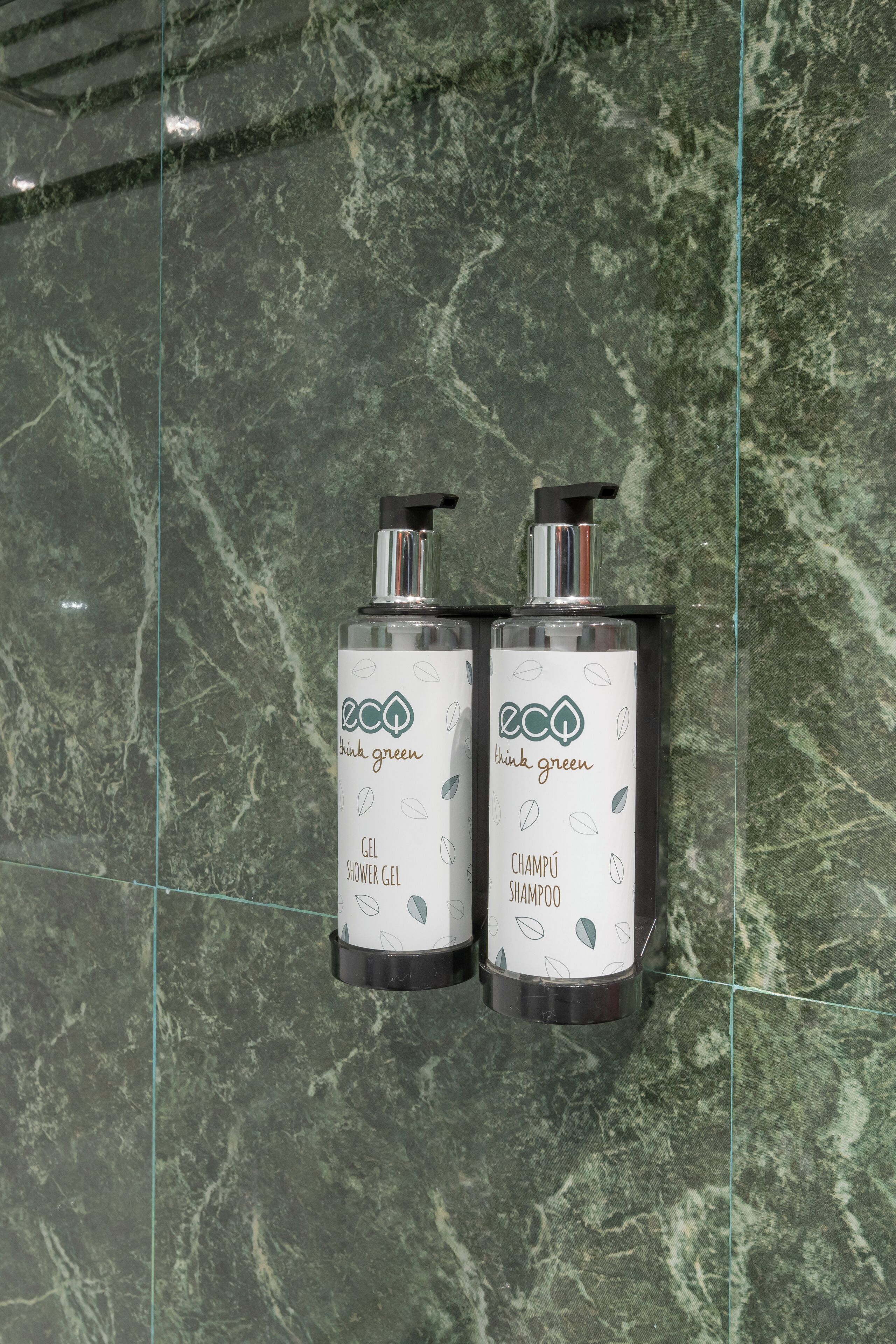 Two bottles of 'think green' shampoo and shower gel on a marble surface.