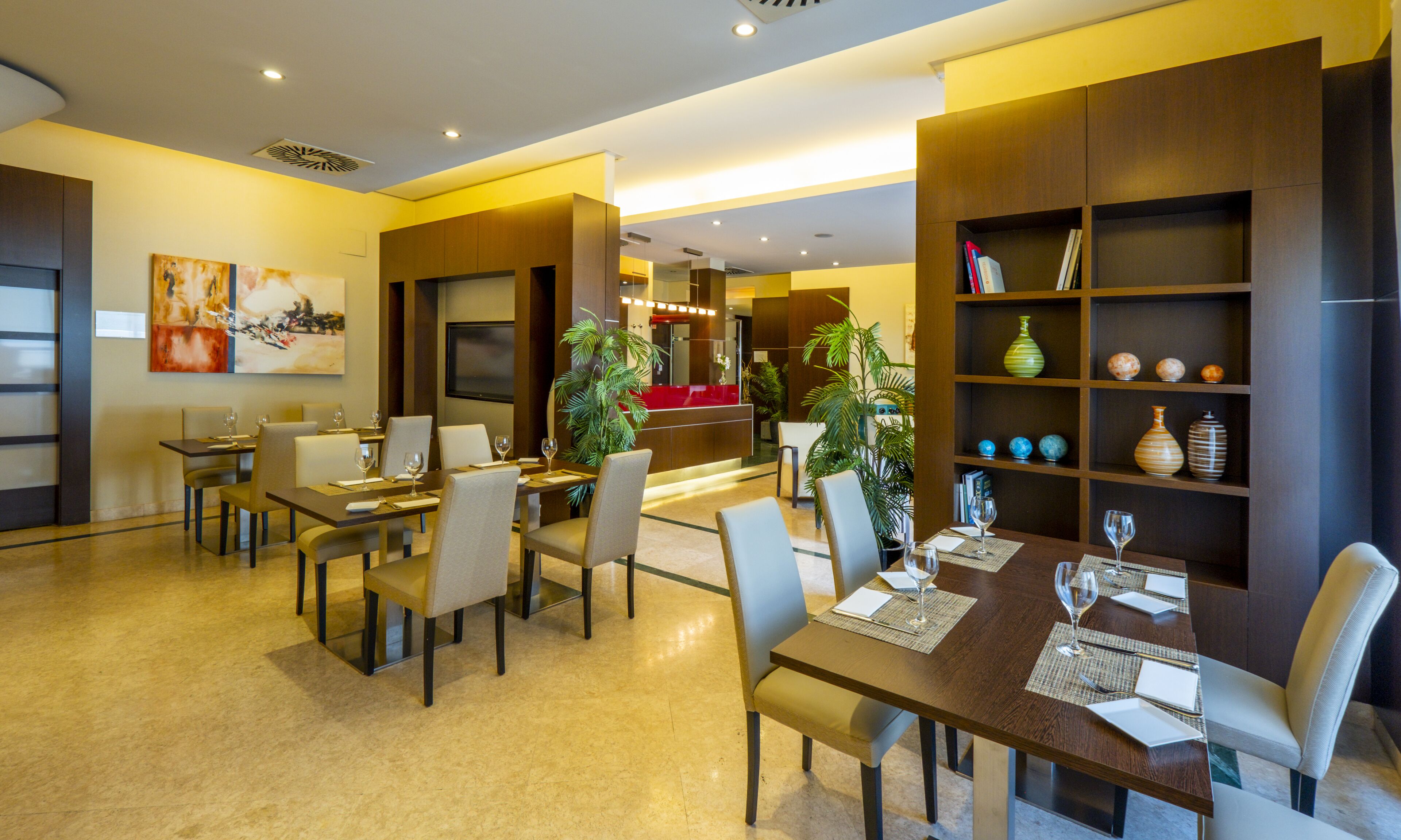 Um espaço de refeições moderno em hotel, com uma mesa comprida, diversas cadeiras e uma receção ao fundo.