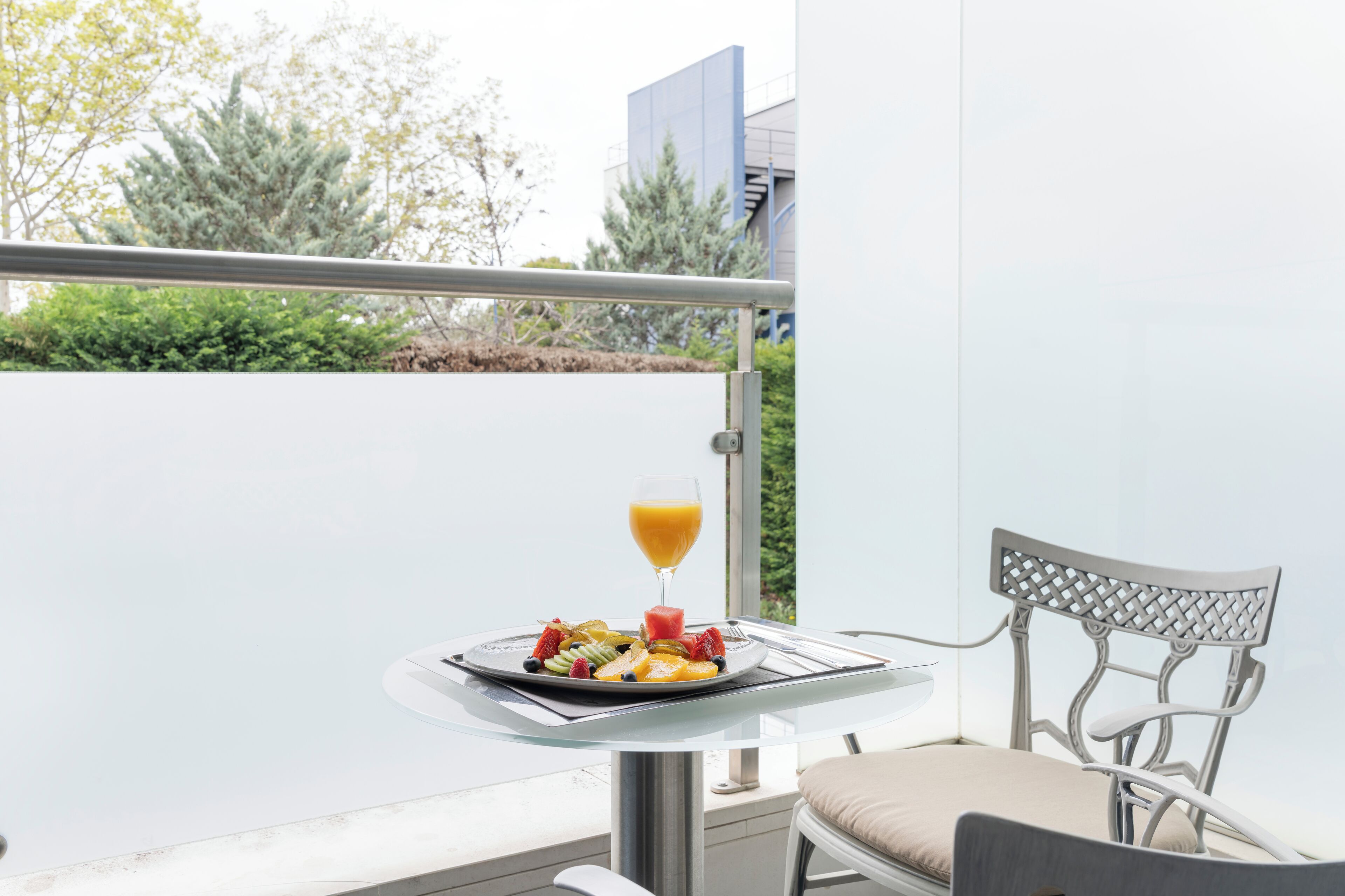 Un balcón con una mesa de comedor, una silla y un plato de fruta y jugo.