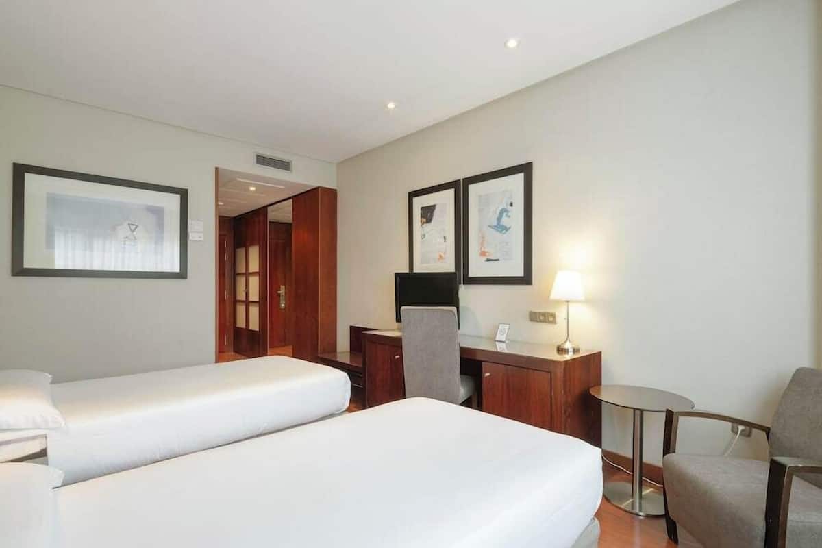 Una habitación de hotel con dos camas, un escritorio, una silla y una mesita.