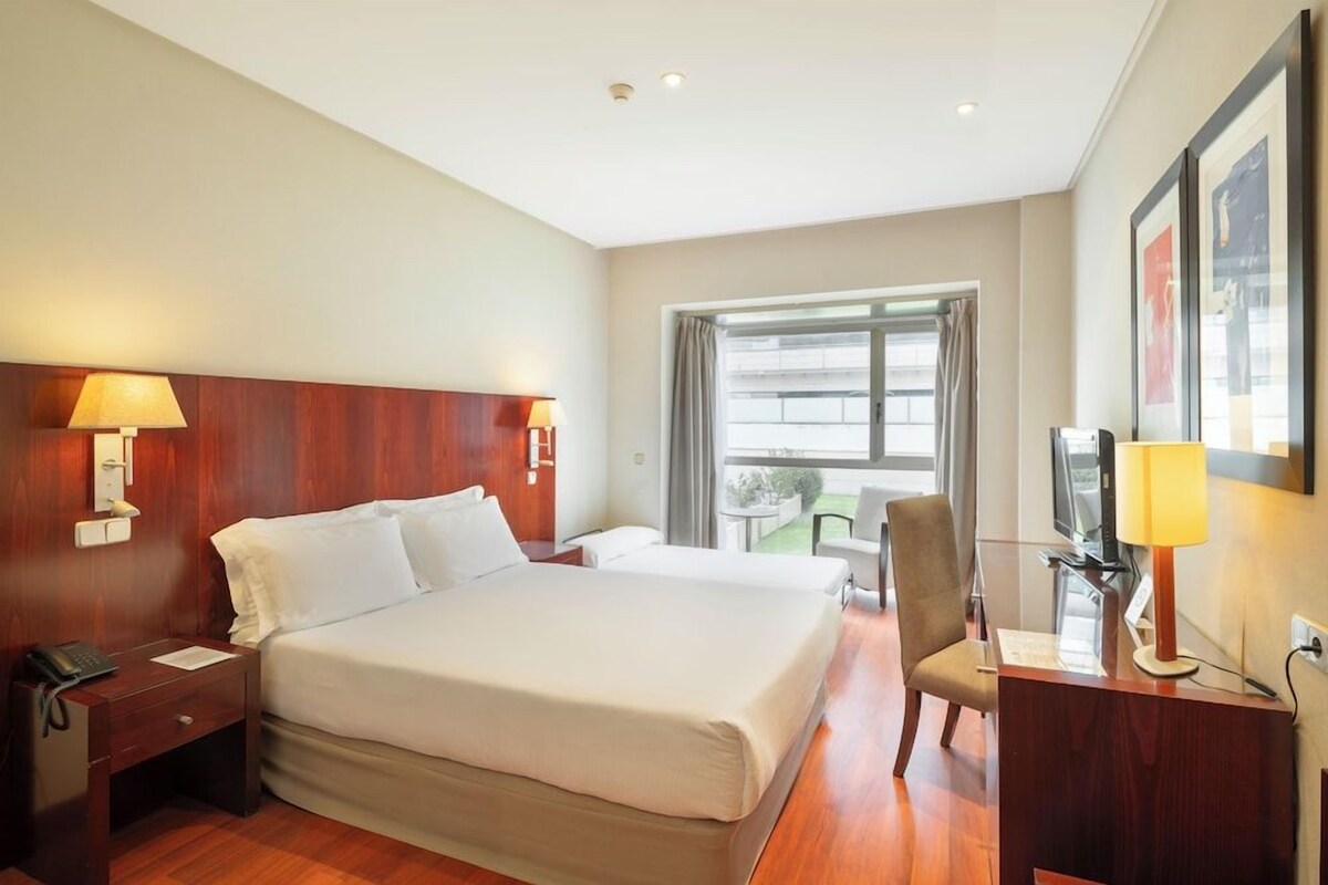 A hotel room with a large bed, bedside lamps, a desk with a television, and a window with curtains.