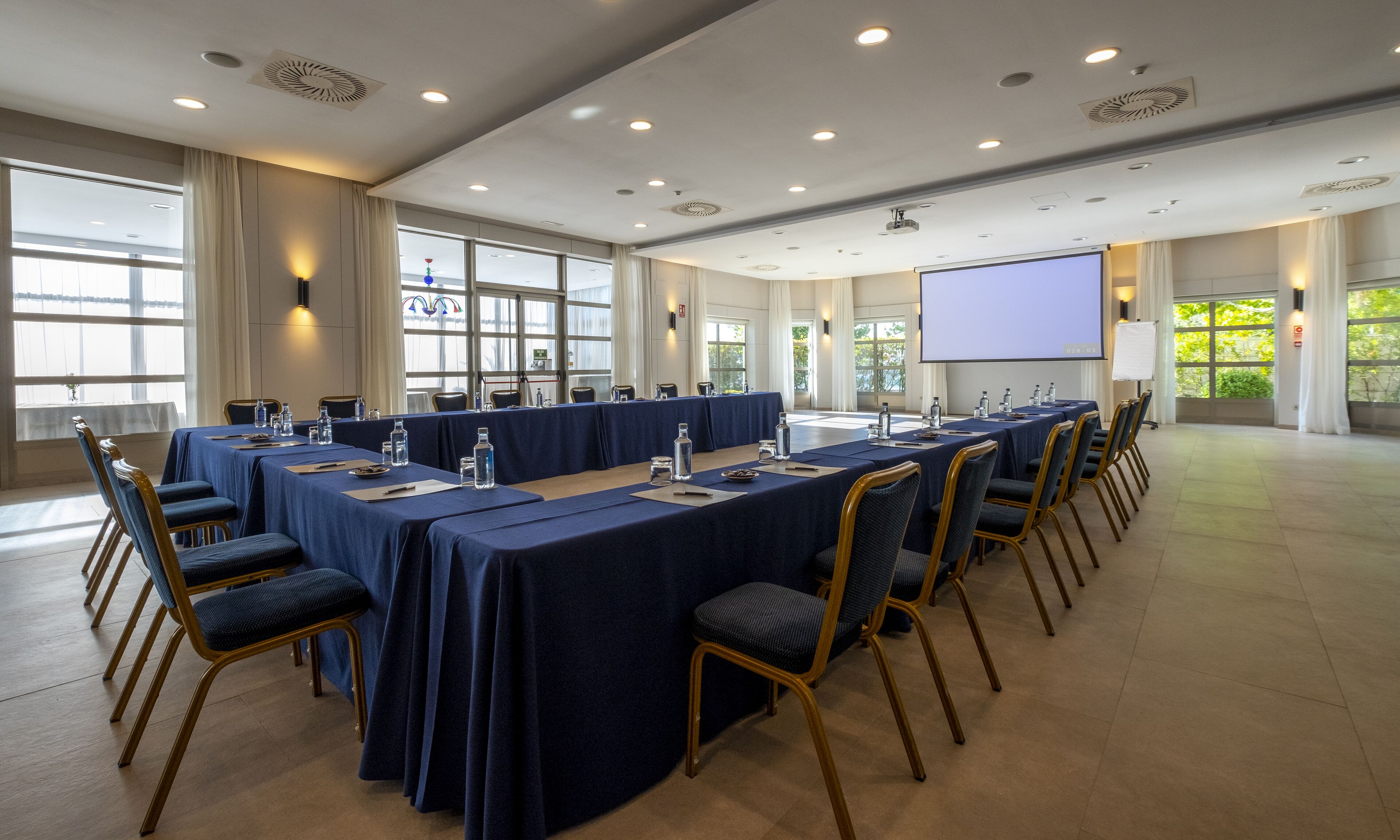 Un salón de conferencias con una larga mesa, sillas y una pantalla de proyector.