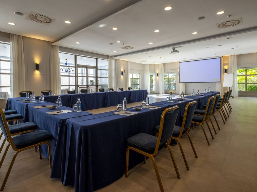 Un salón de conferencias con una larga mesa, sillas y una pantalla de proyector.
