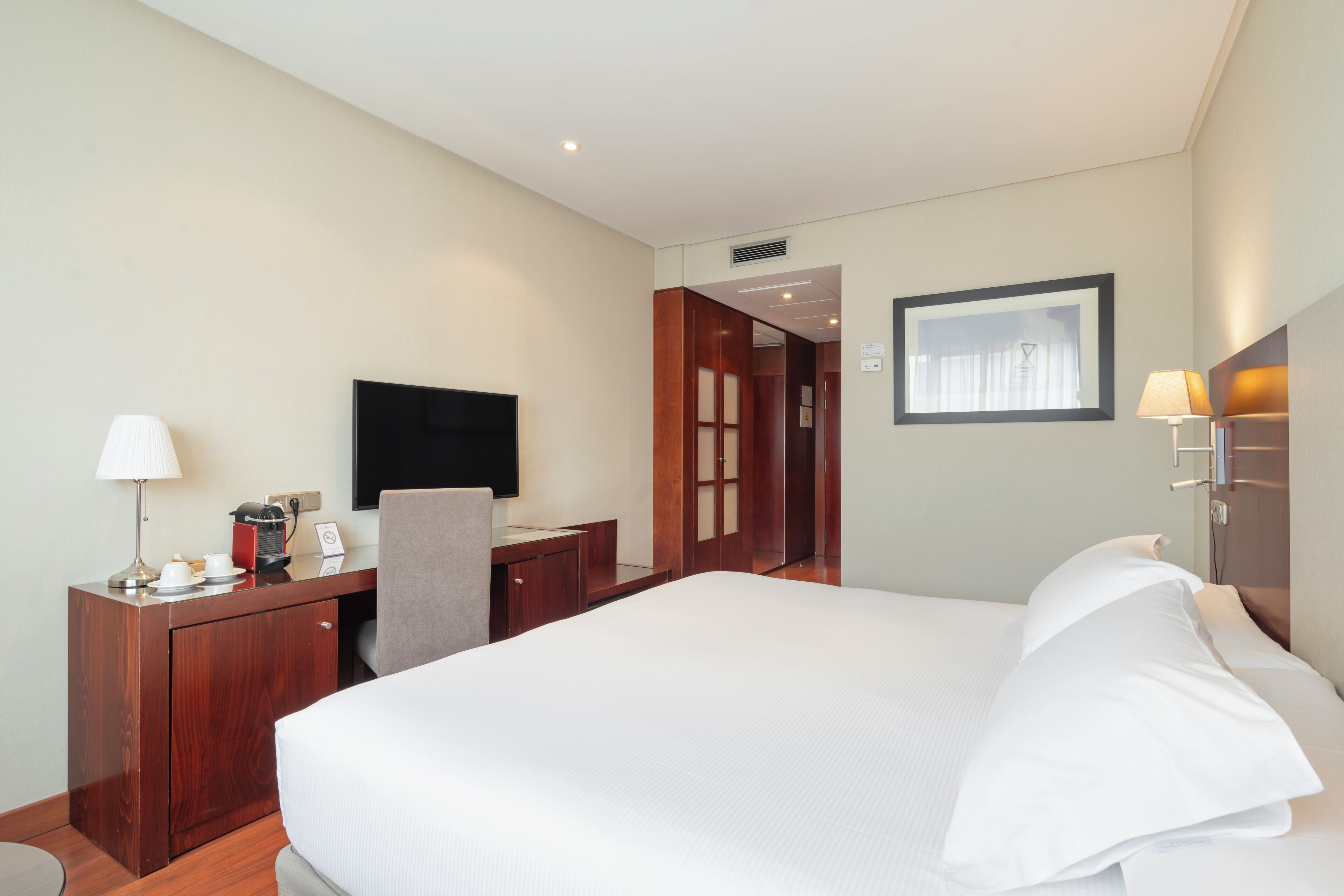 A hotel room with a bed, a desk, a TV, and a door leading to another room.