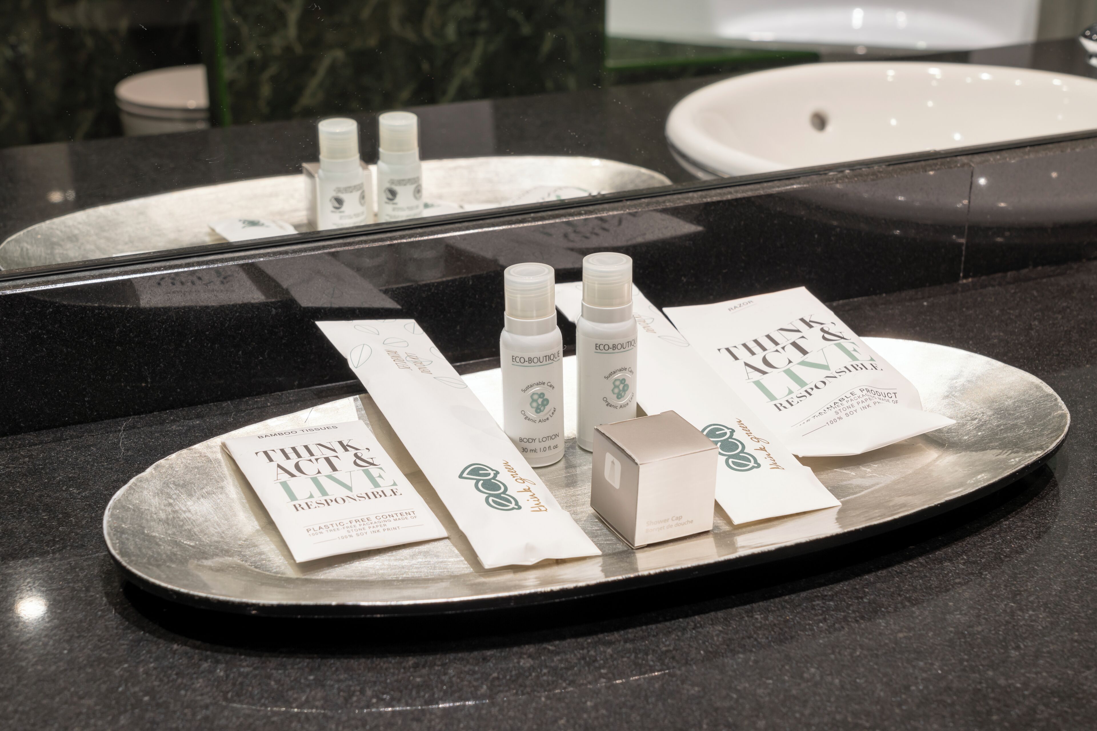 A bathroom counter with a tray containing toiletries and a booklet titled "Think Act Live Responsibly."