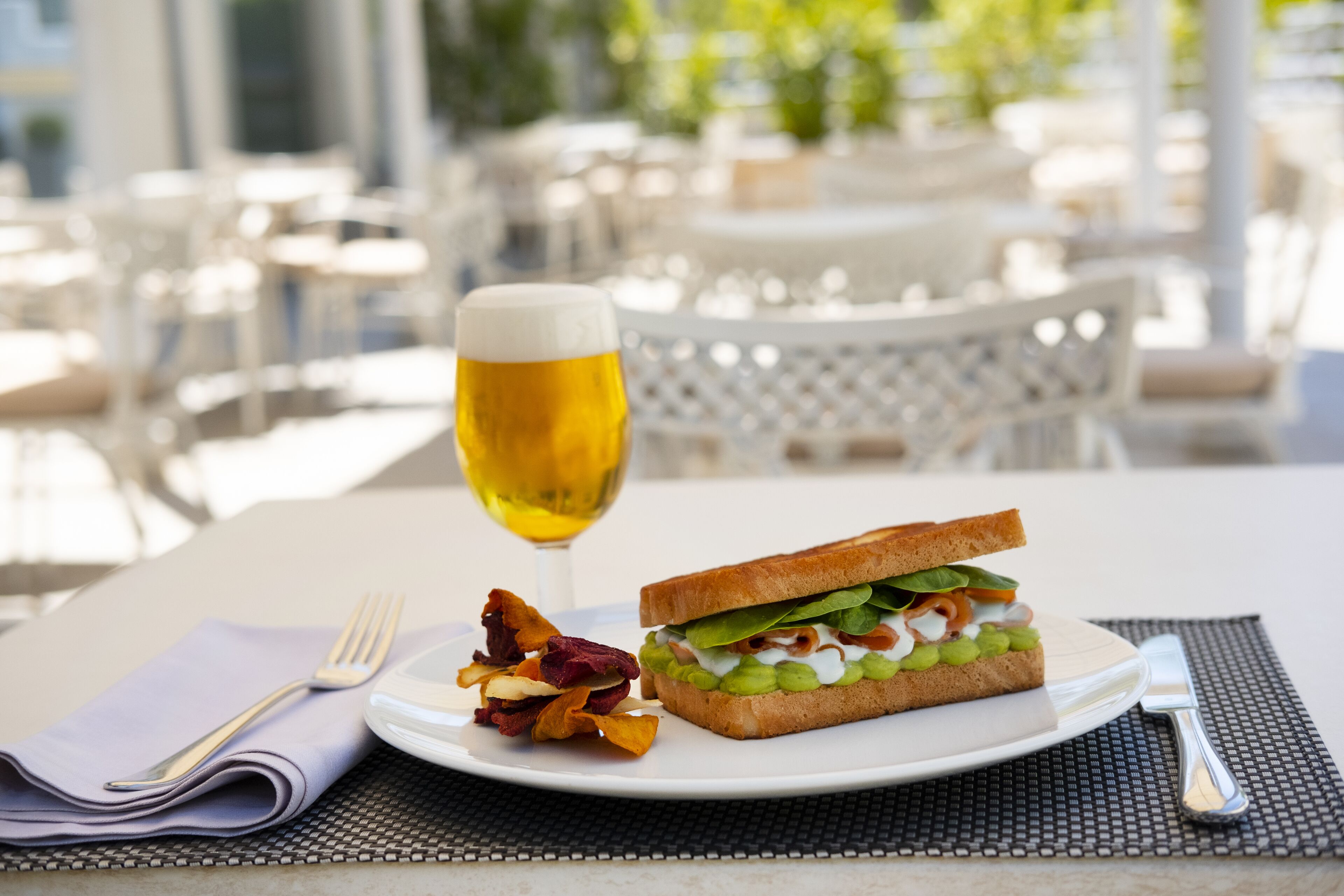 Un plat amb un sandwich, una copa de cervesa i patates com a guarnició sobre una taula.