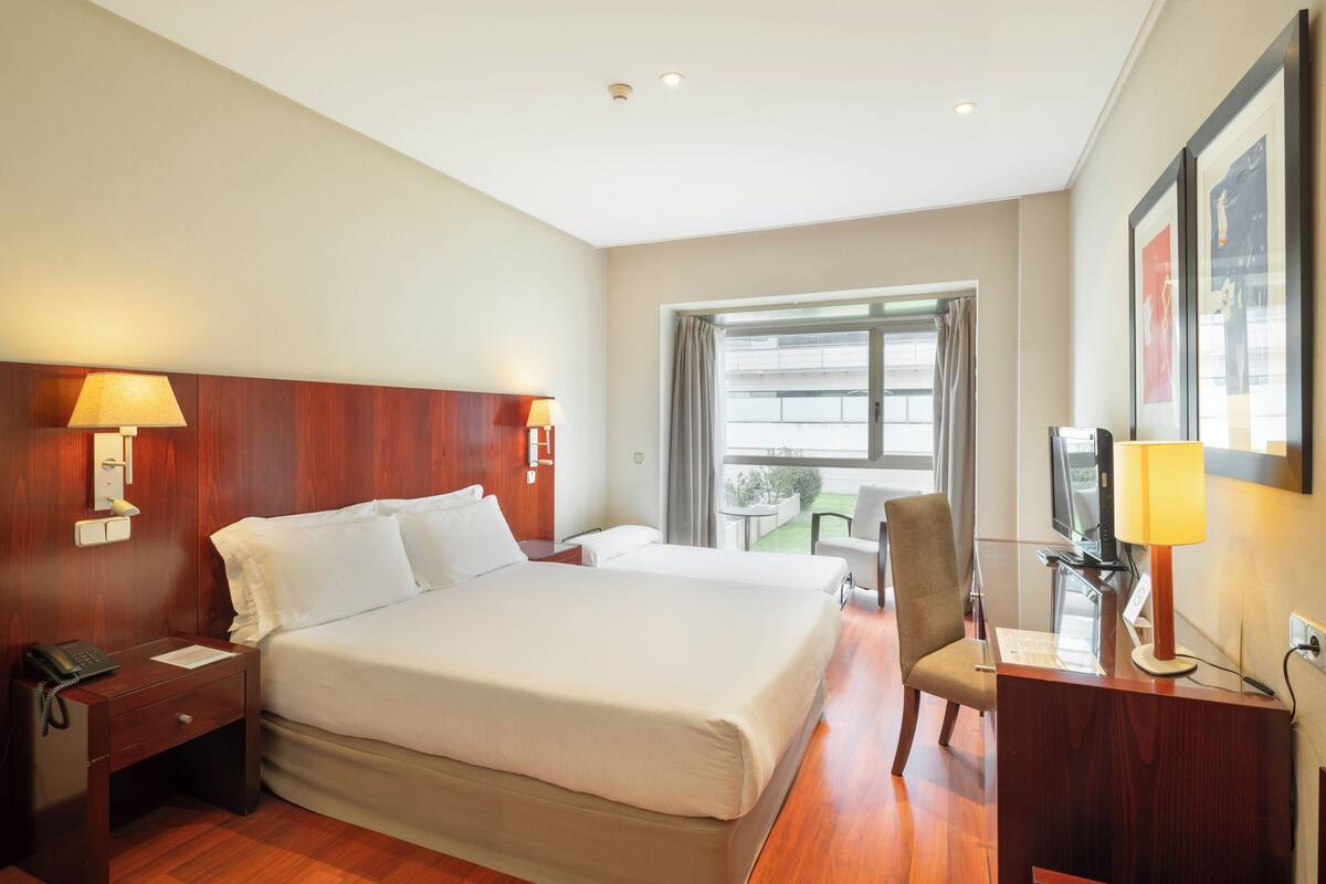 Una habitación de hotel con una cama grande, lámparas de noche, un escritorio con lámpara, una silla y un televisor.
