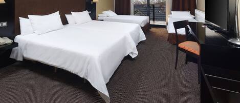 Habitación de hotel con dos camas, un escritorio con silla, televisor y un ventanal con vistas a montañas.
