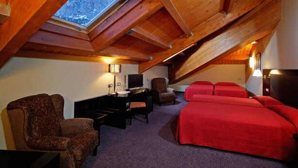 Una habitación acogedora con techo inclinado, un escritorio con computadora, una silla y dos camas con ropa de cama roja.