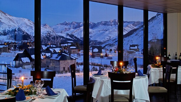 Un restaurante con mesas preparadas para comer, amplias ventanas que ofrecen vistas de montañas nevadas.