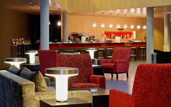 Un área de bar moderna con sillas tapizadas en rojo, una barra con equipo y un rincón de estar con mesa y sillas.