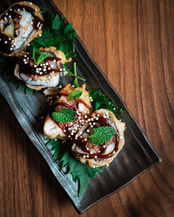 A sushi dish with sesame seeds and green leaves on a dark plate. - SH Villa Gadea Hotel (Altea)
