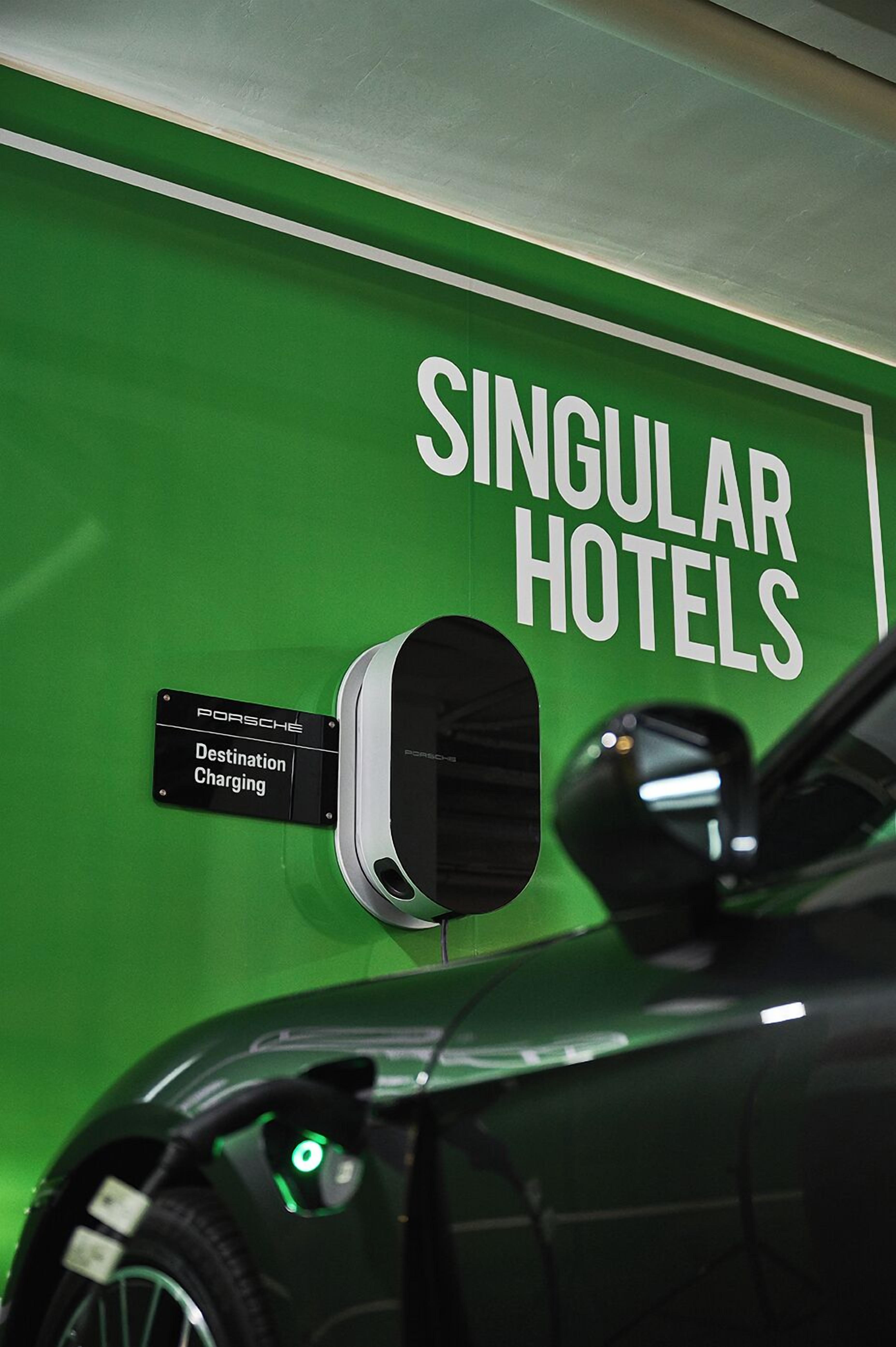 A green wall with a sign for Singular Hotels and a destination charging sign for a Porsche.