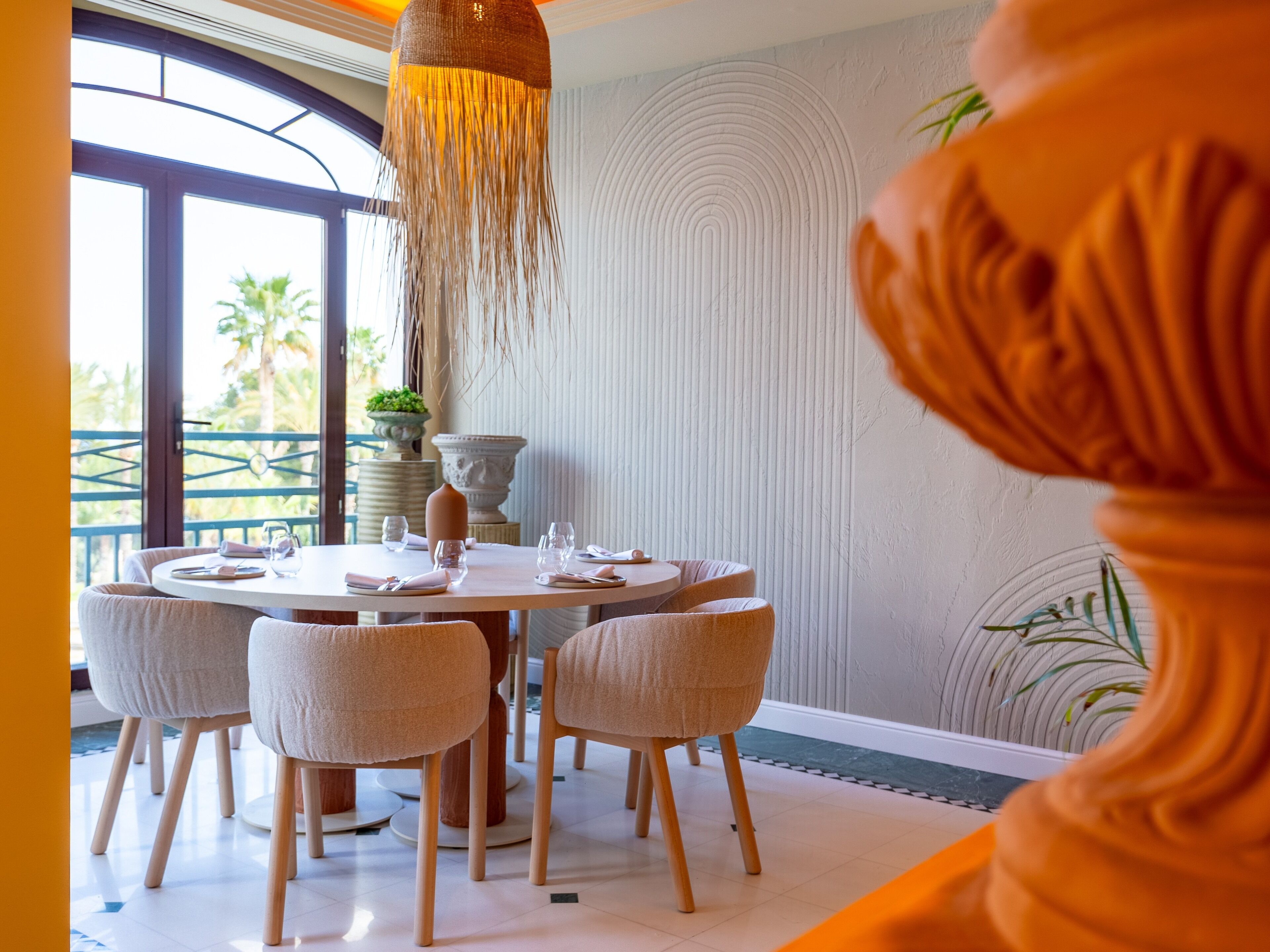 A dining area with a round table, six chairs, and a hanging light fixture.