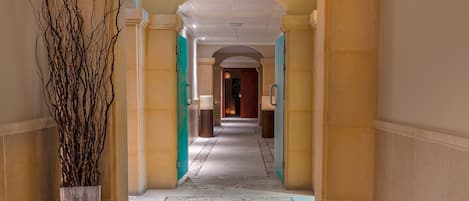 A corridor with a tiled floor, a large vase with branches, and a door at the end.