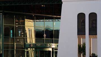 A modern hotel with a glass facade, a metal roof, and a sign reading "HOTEL VILLAGE".