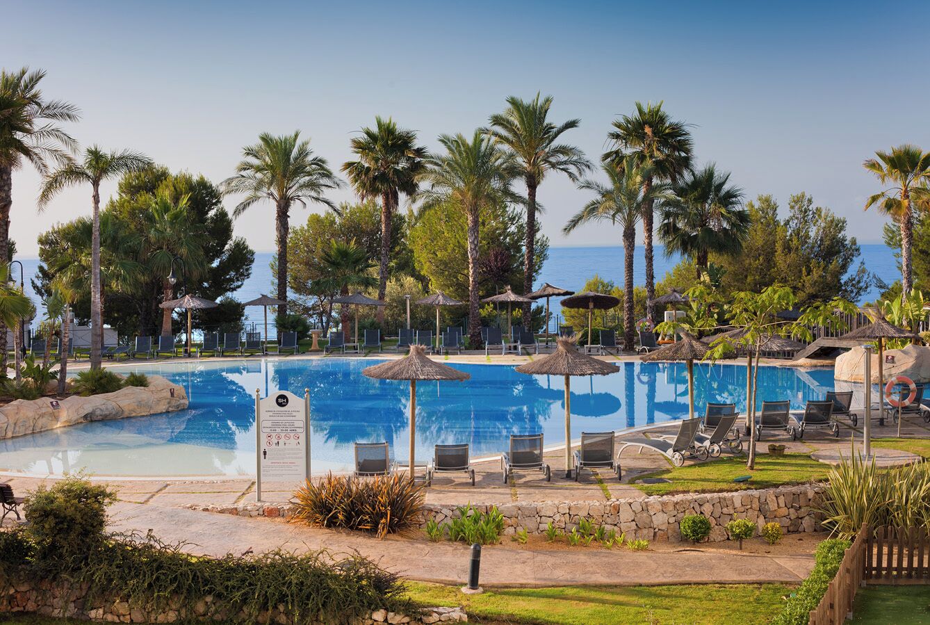 Zona de piscina con sillones de descanso, palmeras y vista despejada al mar.