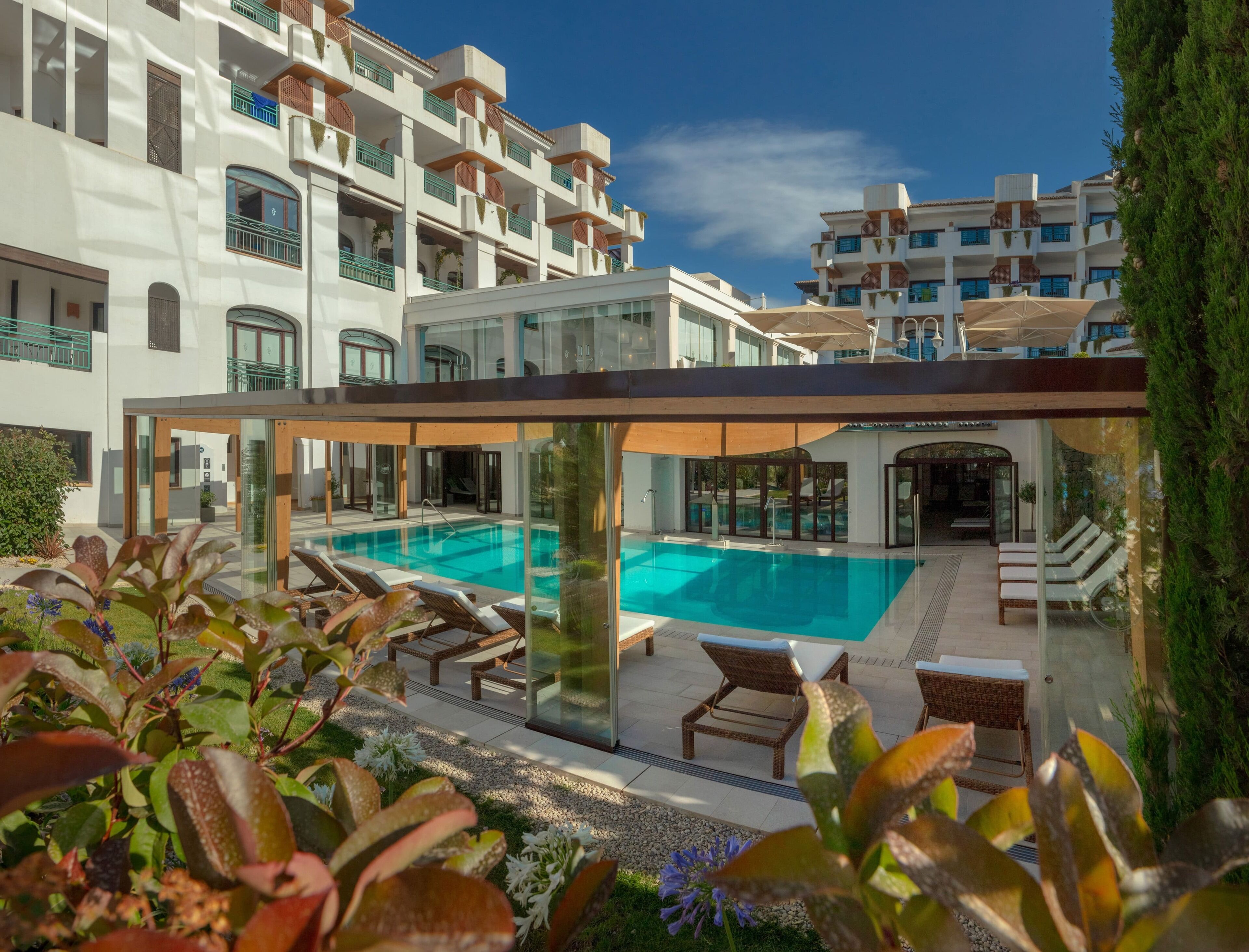 Un hotel moderno con area piscina, sdraio e zona relax coperta.