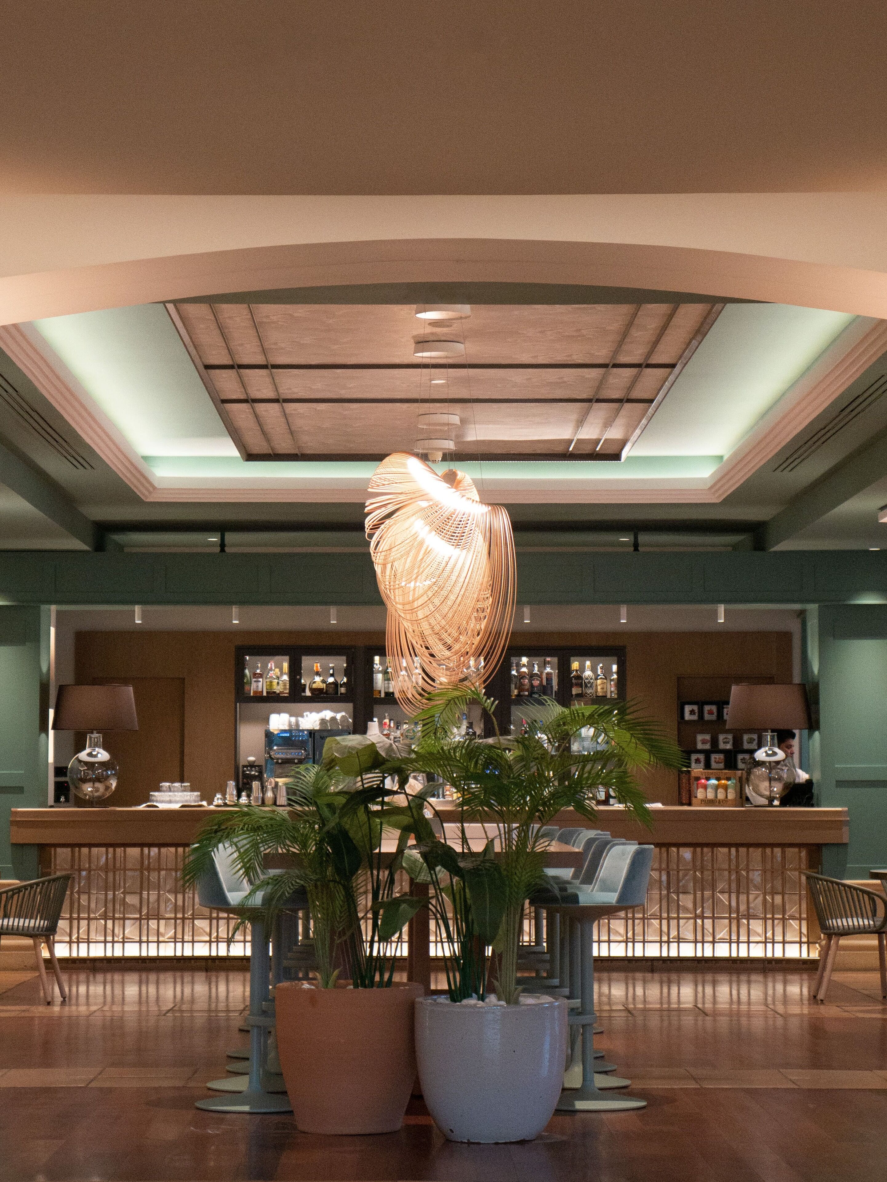 A lobby with a central bar area, potted plants, and a unique hanging light fixture.