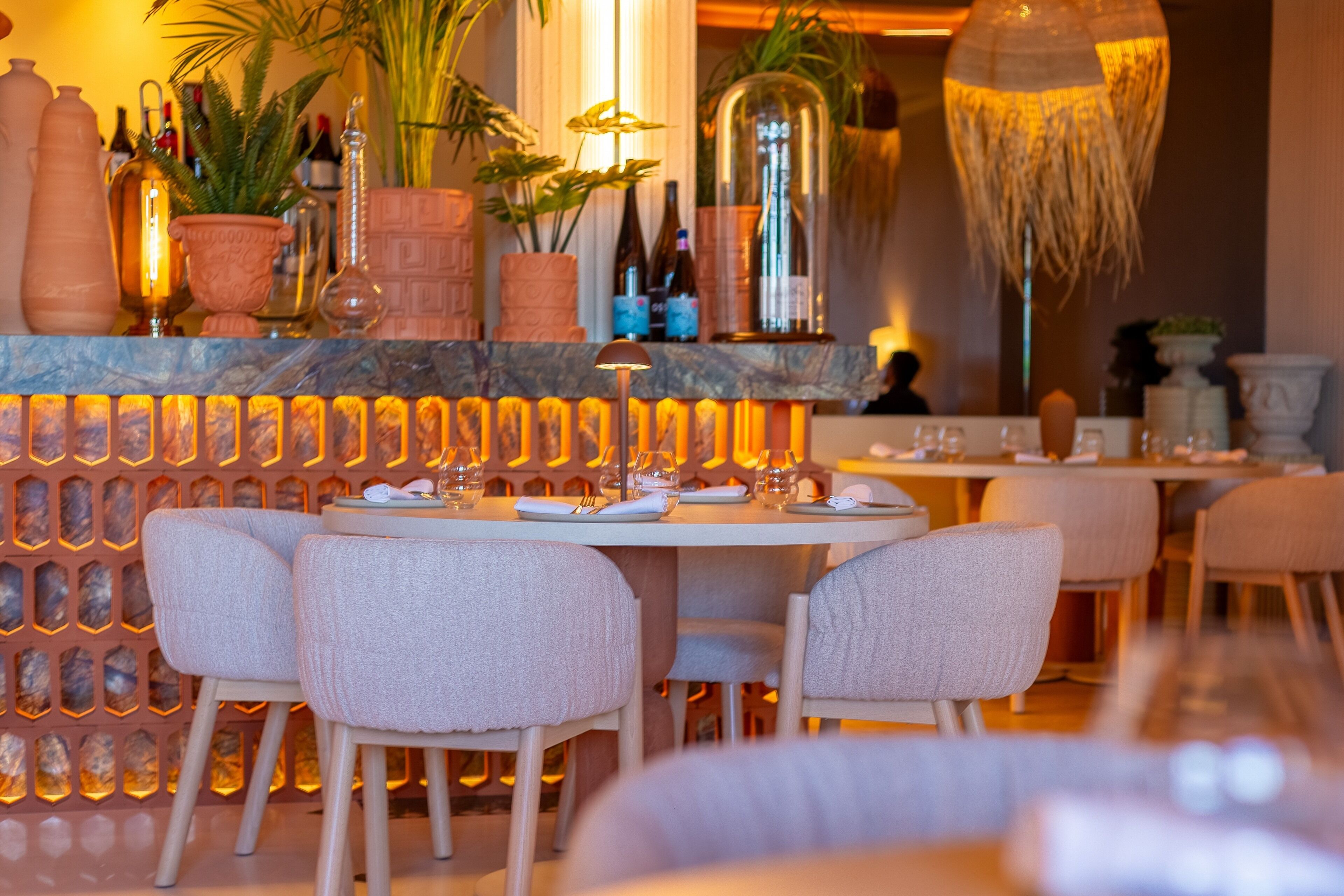 Un restaurante con barra de mármol, sillas acolchadas y una variedad de botellas y plantas en los estantes.