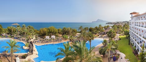 A resort with multiple swimming pools, palm trees, and a view of the sea.