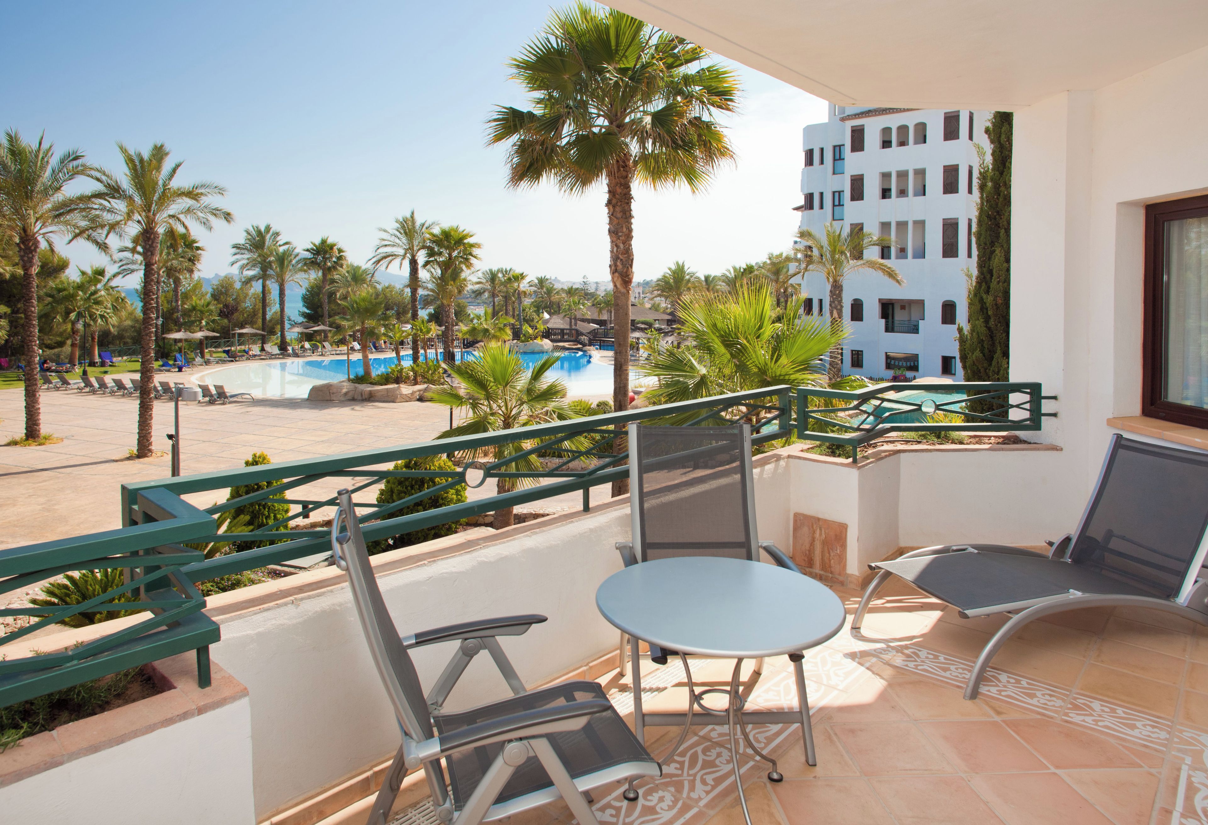 Un balcón con vista a la piscina, mobiliario exterior y una vista del edificio de un hotel.