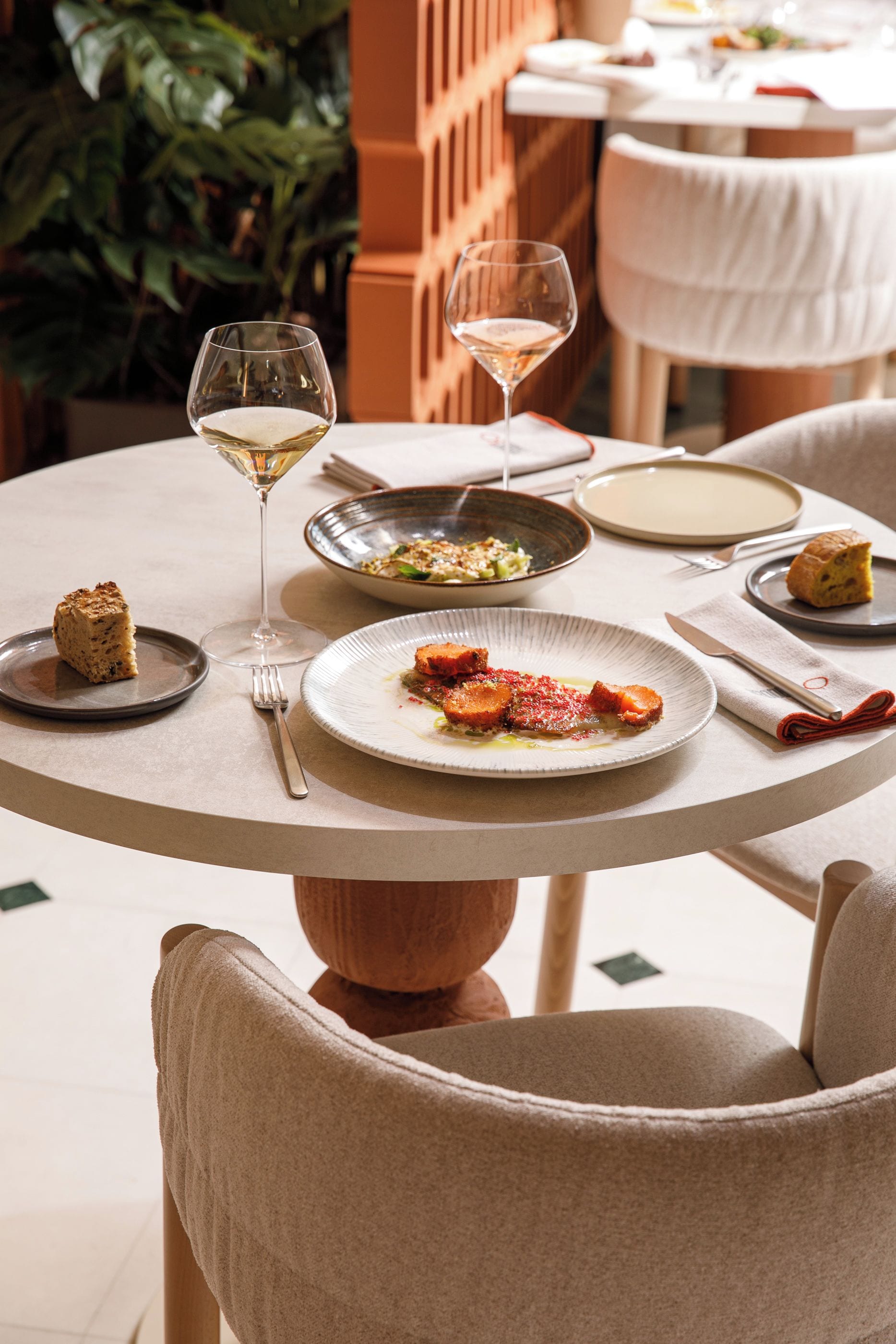 A round dining table with plates of food, glasses of wine, and cutlery.