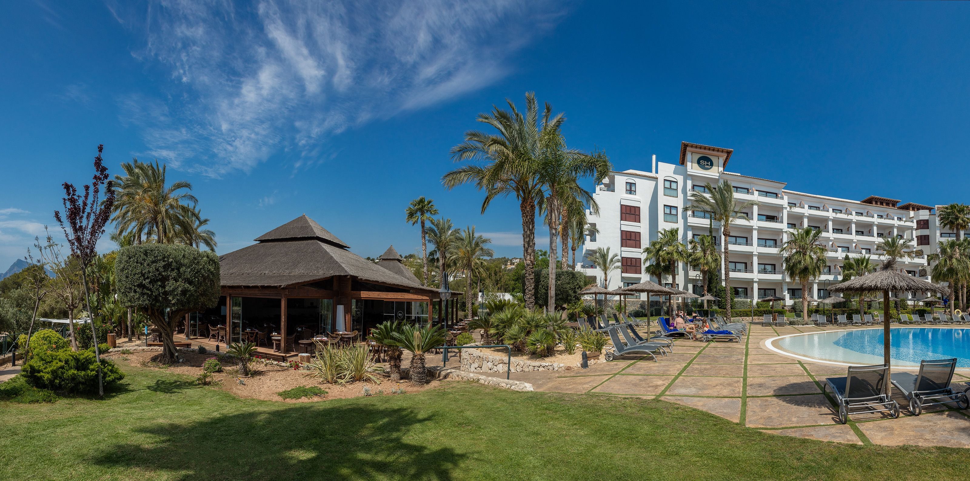 A resort with a pool, lounge chairs, palm trees, and a building with balconies.