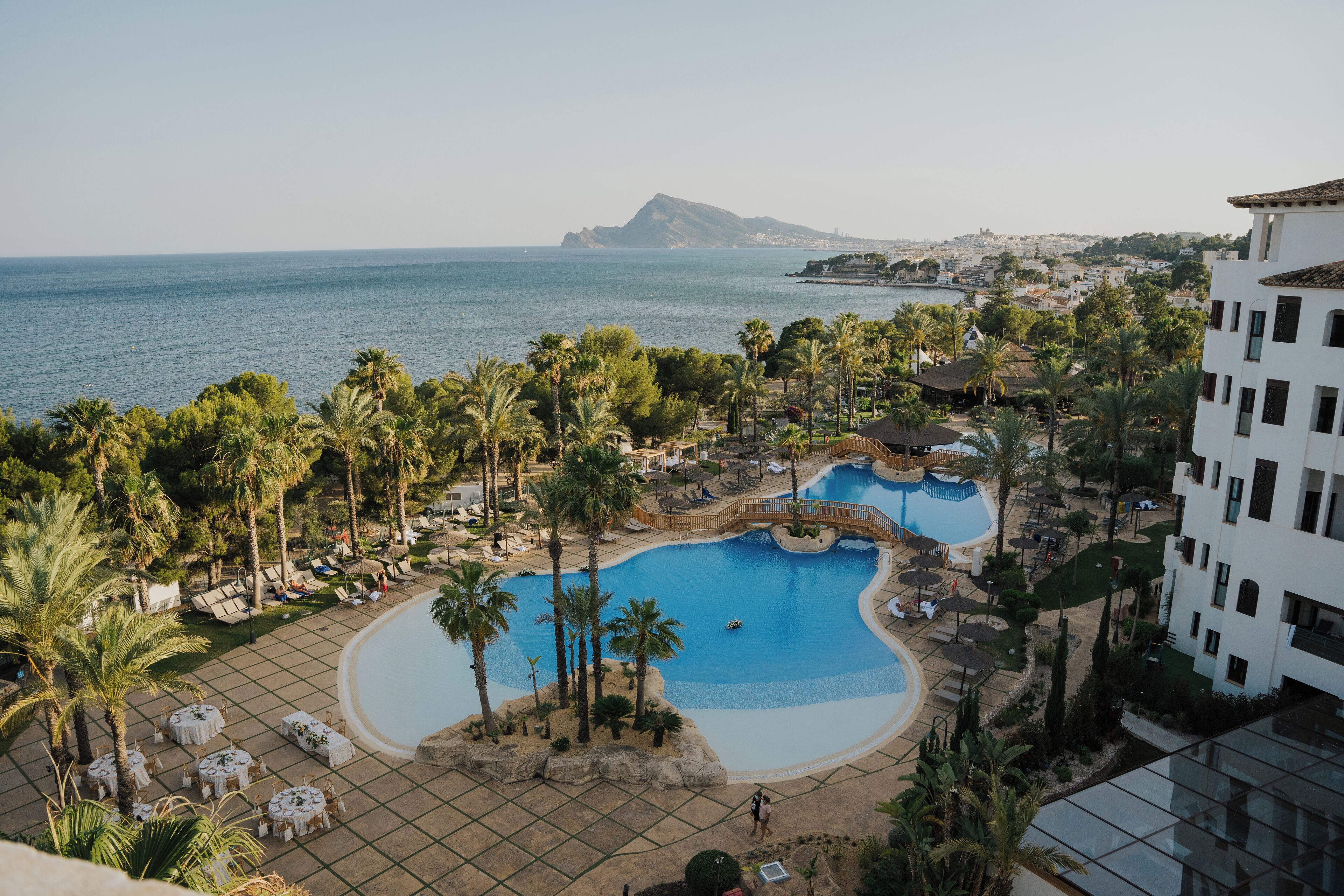 A resort with a large pool, palm trees, and a view of the sea.