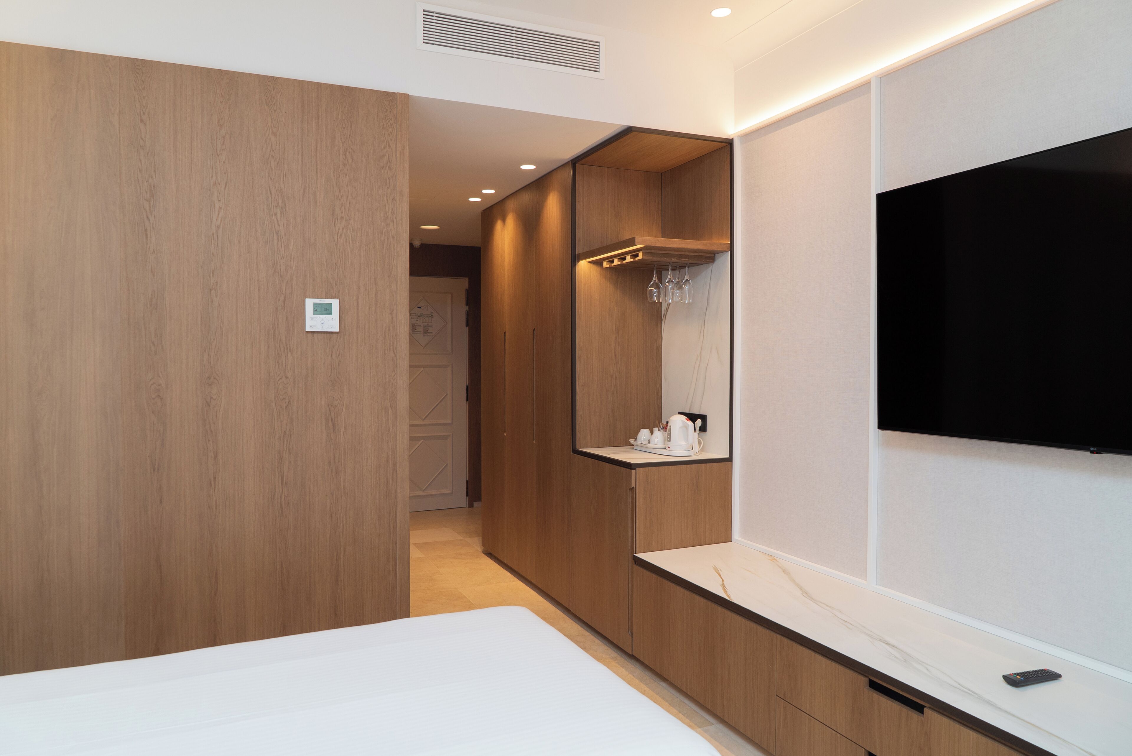 A modern hotel room with a wooden wardrobe, a built-in TV, and a small shelf with toiletries.