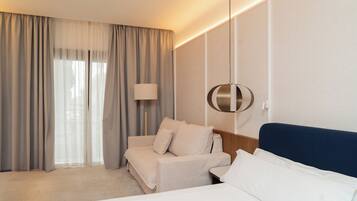 A hotel room with a bed, a sofa, a lamp, and a wall-mounted light fixture.