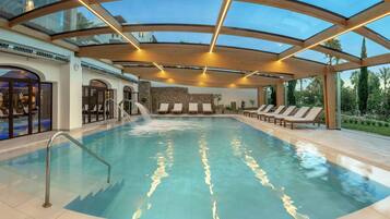 Una piscina interior con techo de vidrio, sillas de descanso y una pared de piedra.