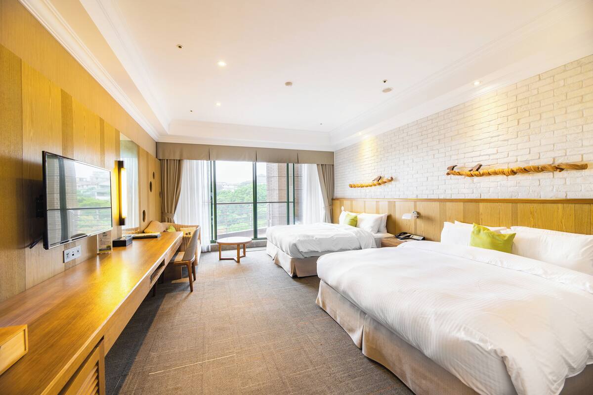 Habitación de hotel con dos camas, un escritorio, un televisor y una pared de ladrillo.