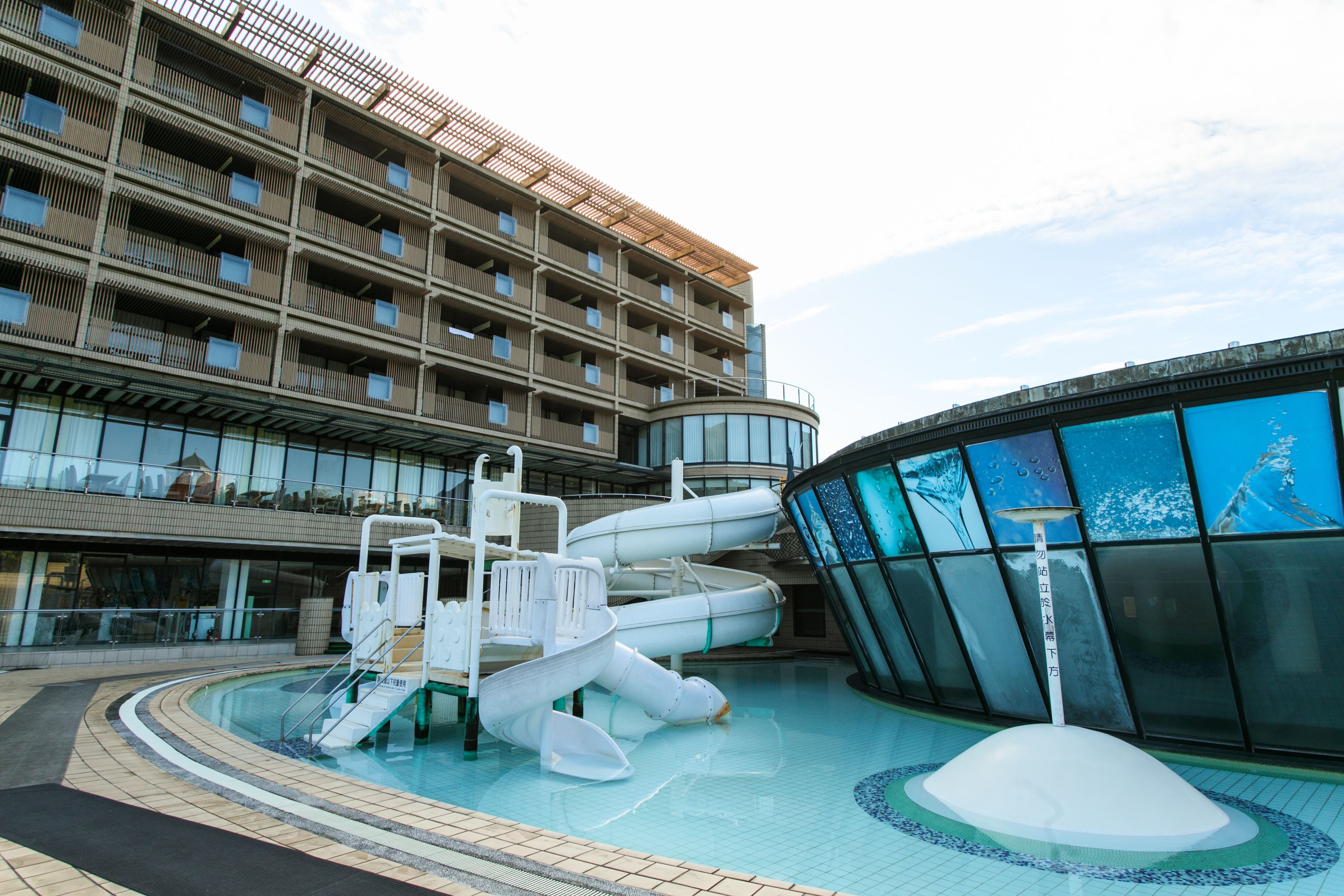 A modern hotel with a pool area featuring a water slide and a circular glass structure.
