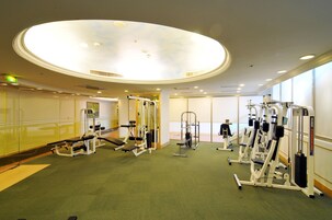Un gimnasio con diversas máquinas de ejercicio, piso cubierto de moqueta verde y un tragaluz circular grande.