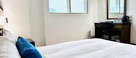 Habitación de hotel con una cama grande, un escritorio con silla, un espejo y una ventana con vistas.