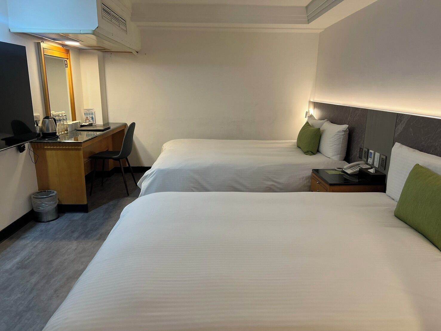 A hotel room with two beds, a desk with a chair, a trash bin, and a minibar.
