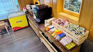 Zona de recepción de un hotel con una máquina de café, un pequeño espacio para sentarse y una exhibición de aperitivos envasados.
