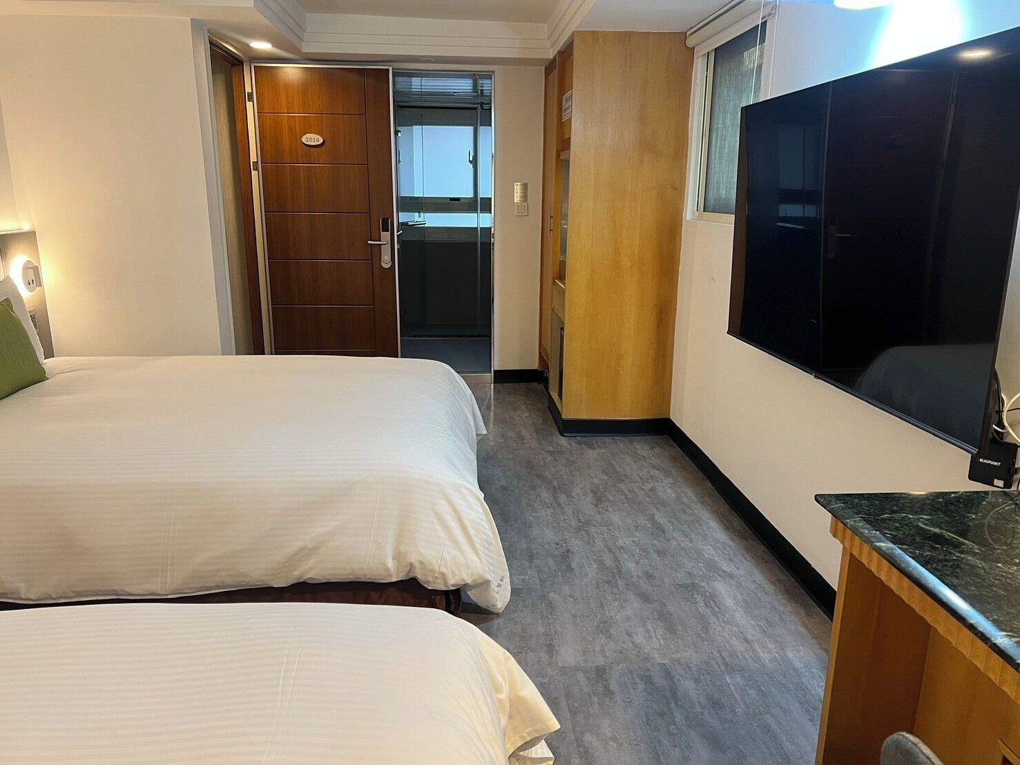 Ett hotellrum med två sängar, en TV, en garderob i trä och en dörr som leder till ett badrum.