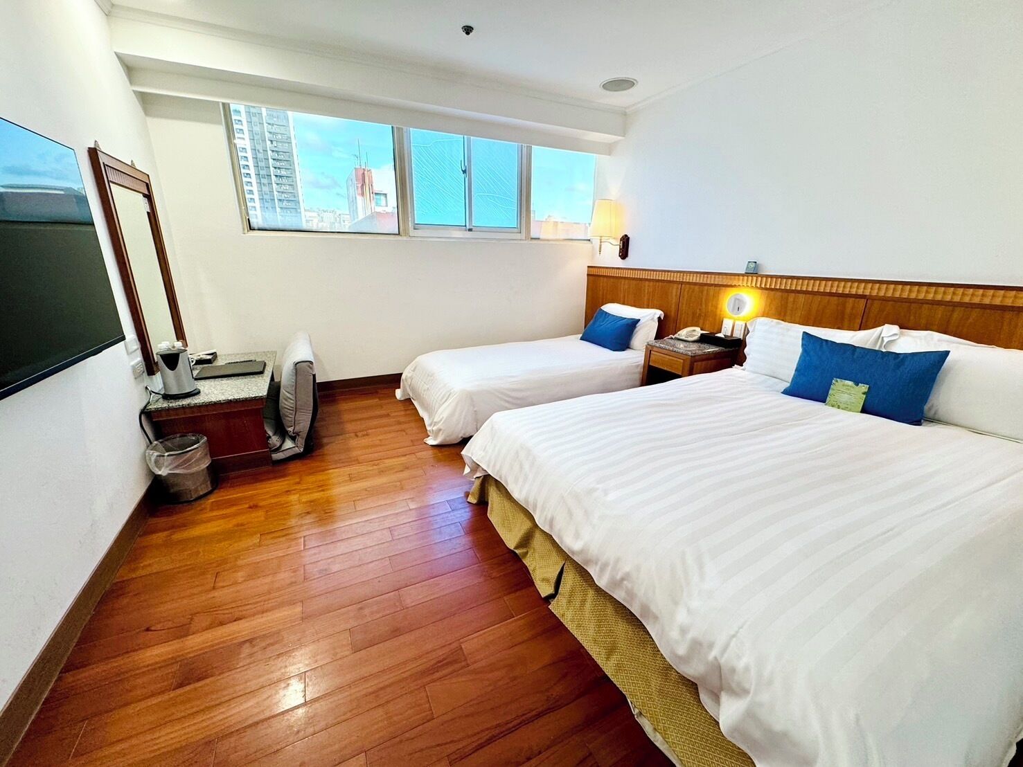 Habitación de hotel con dos camas, un escritorio, una silla, un televisor y una ventana con vistas a la ciudad.