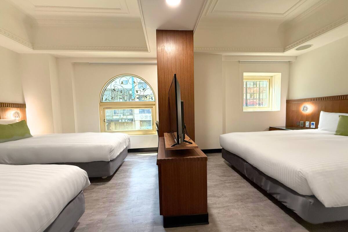 A hotel room with two beds, a TV stand, and a large arched window.