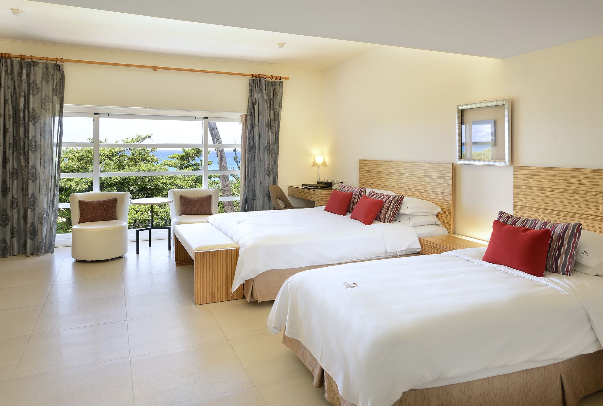 A hotel room with two beds, a chair, a desk, and a large window with curtains.