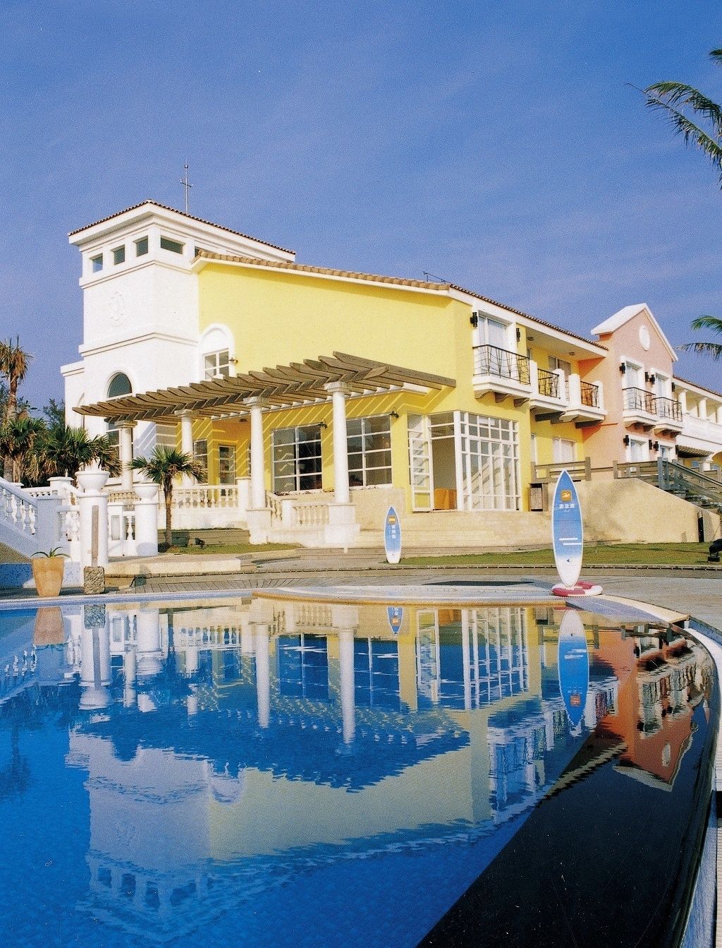 A hotel with a pool, a covered patio, and a two-story building with balconies.